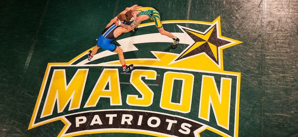 Two wrestlers grappling at center mat on the Mason Patriots logo